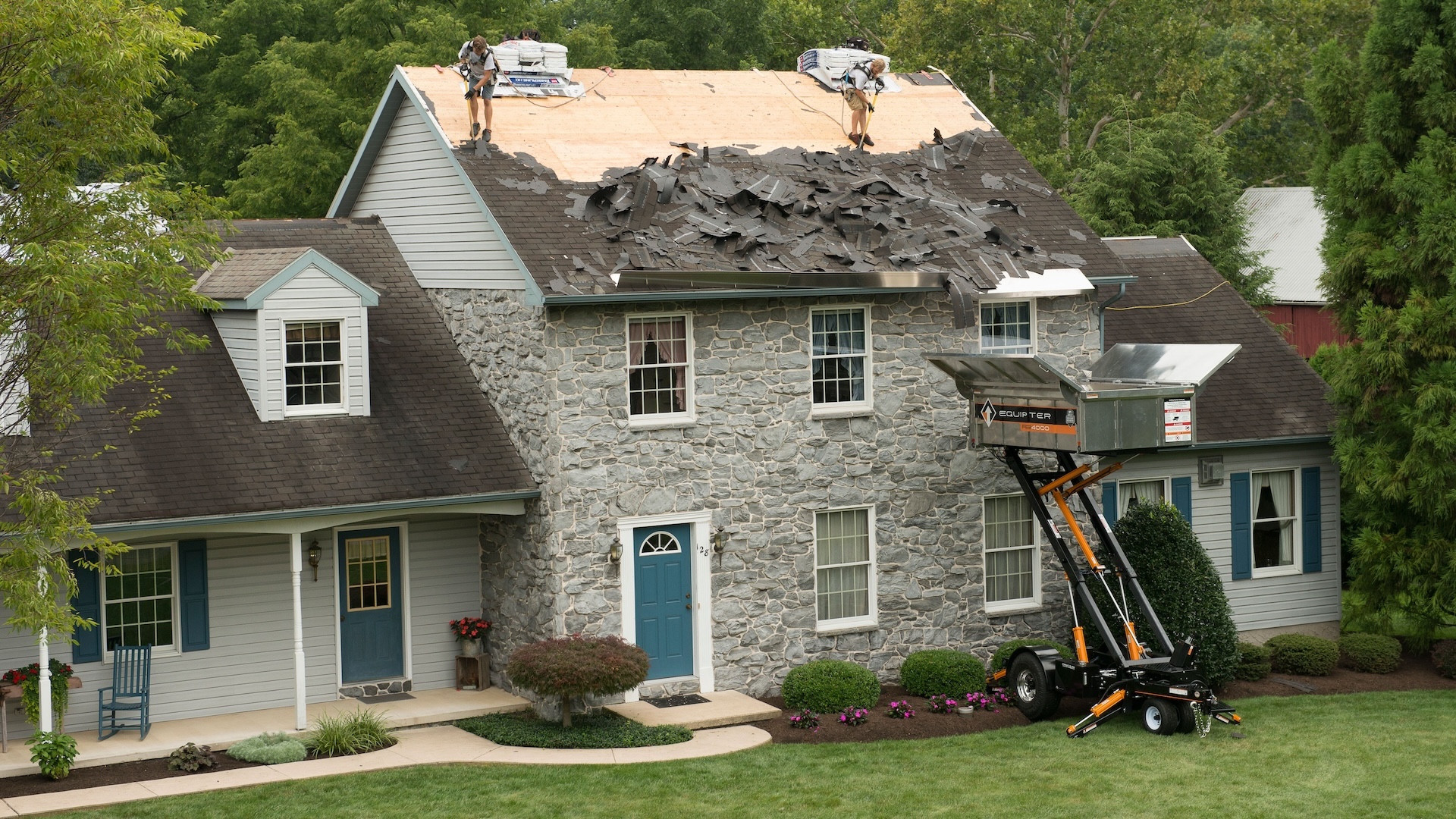 Residential roofers in safety gear feed rooftop debris into Equipter RB4000 during tearoff
