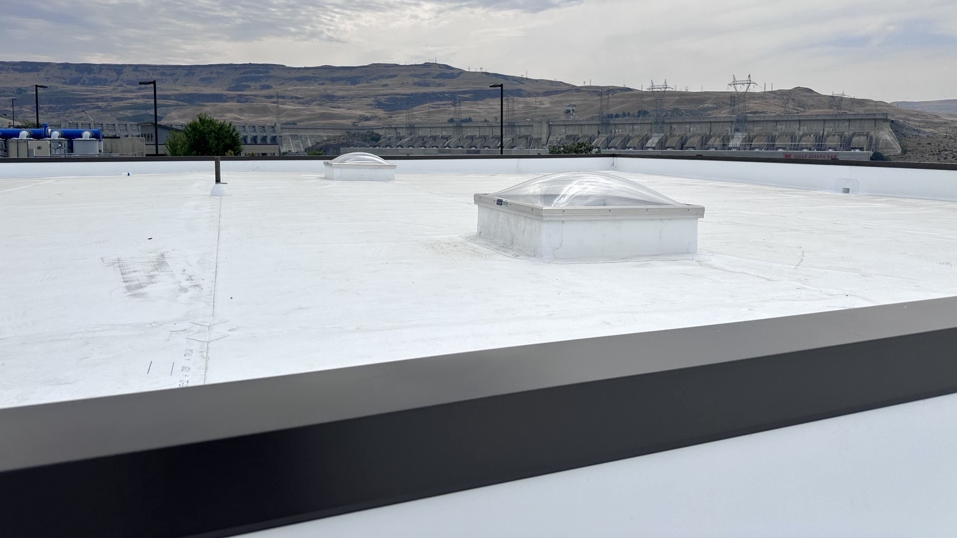 Chief Joseph Hatchery Building Roof (foreground), Dam, And Rugged Landscape (background)